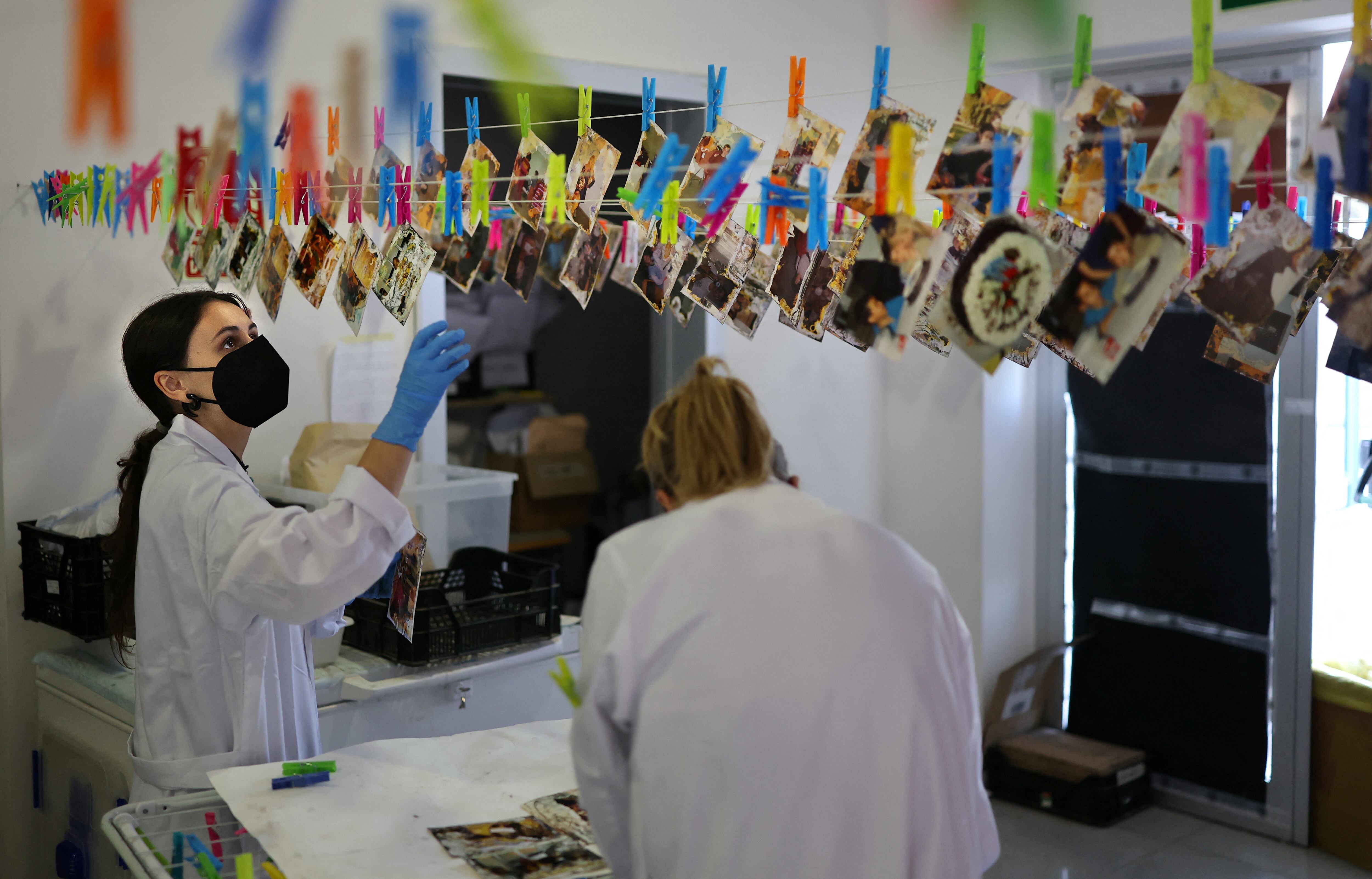 Estudiantes de la Universidad de Bellas Artes de Valencia, el 2 de octubre de 2025, trabajan en la restauración de fotografías familiares dañadas por el lodo durante las inundaciones, colgándolas en tendederos. La Universidad de Valencia está a cargo de un importante proyecto para limpiar y restaurar las fotografías que las familias perdieron durante las trágicas inundaciones del 29 de octubre de 2024, que causaron la muerte de más de 230 personas. (Foto de Thomas COEX / AFP)