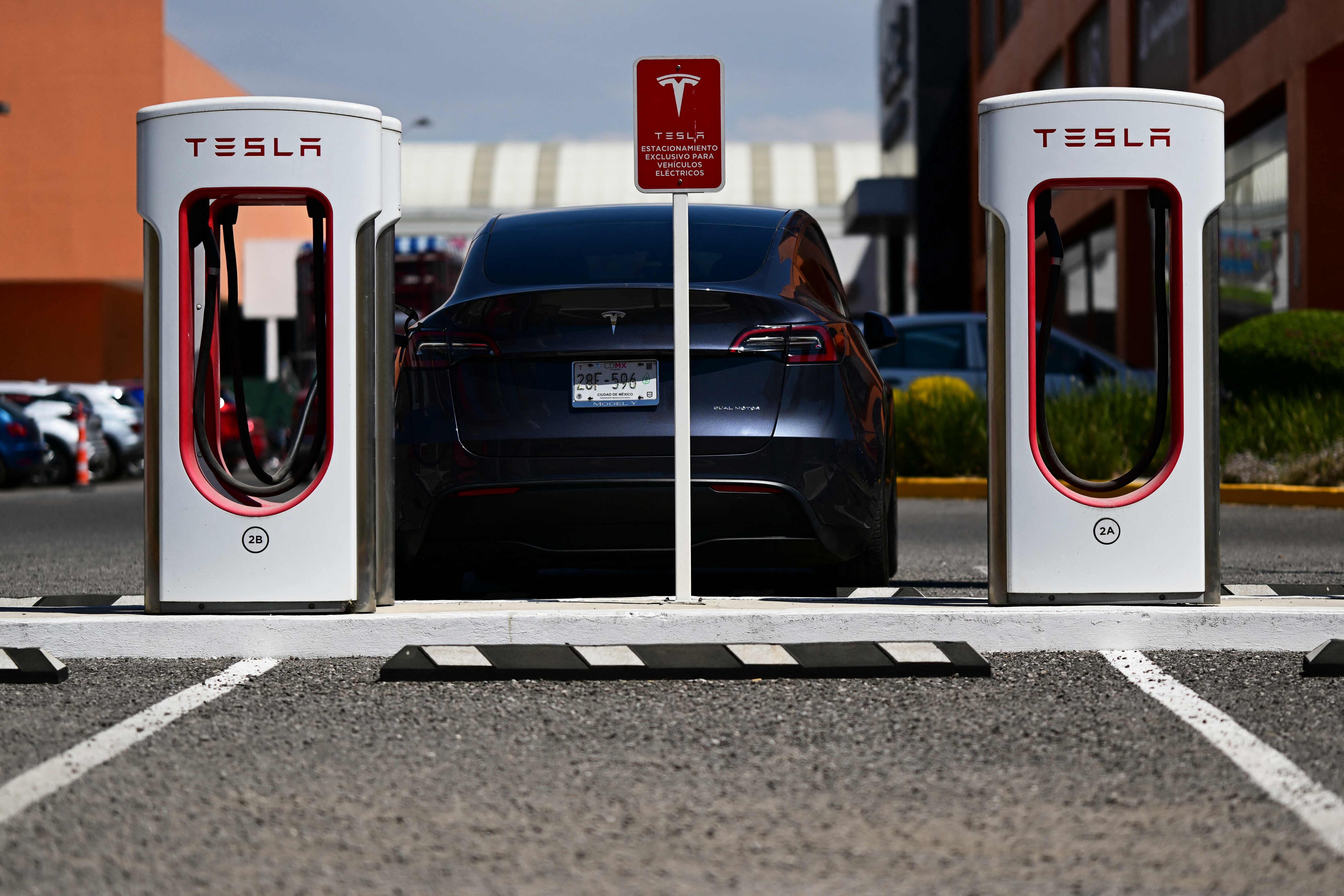 Automóvil Tesla Model Y cargándose en una estación eléctrica con dos cargadores Tesla Supercharger, en un estacionamiento exterior.