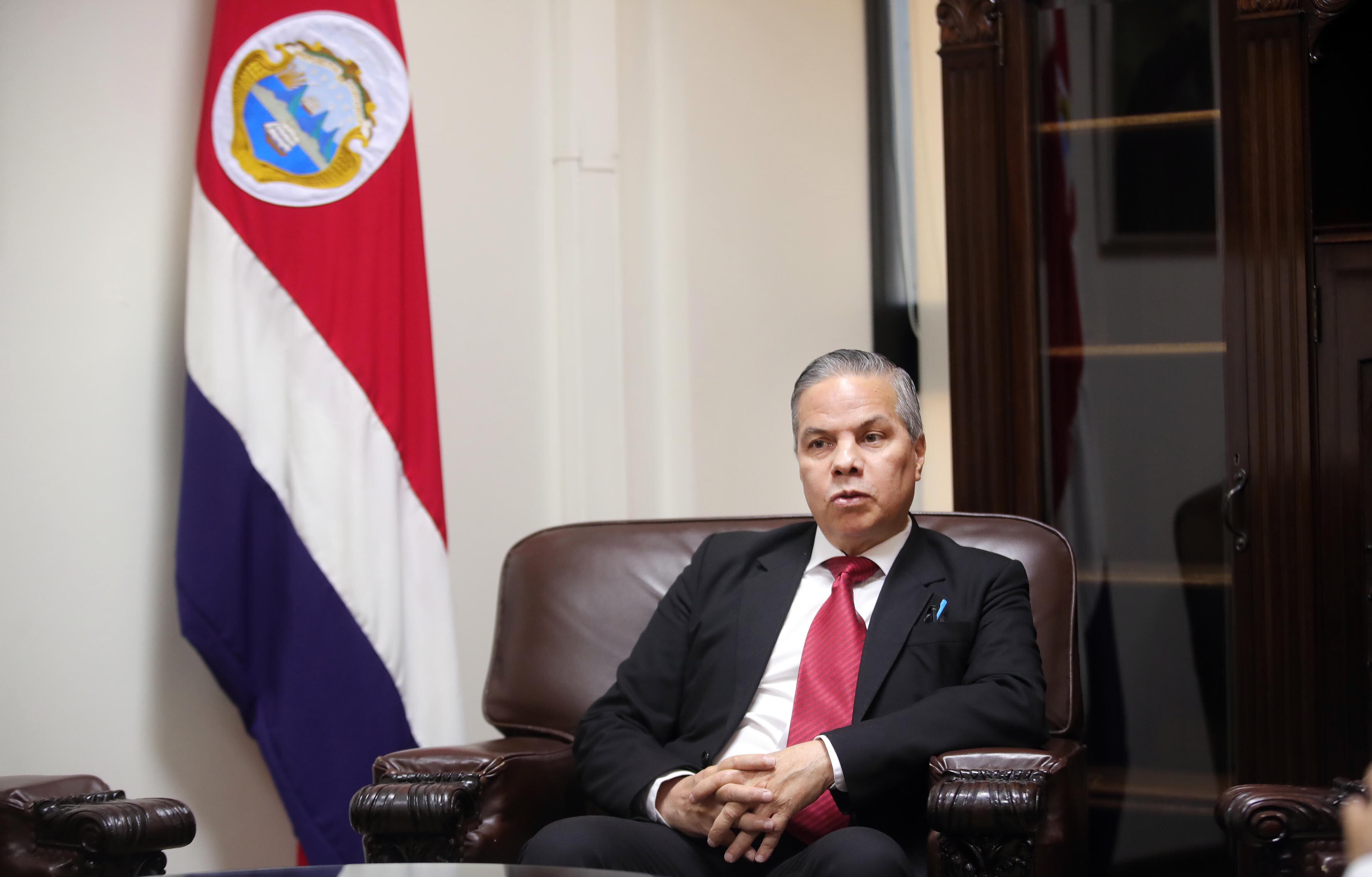 Róger Madrigal, presidente del Banco Central de Costa Rica, sentado en un sillón de cuero frente a la bandera nacional.