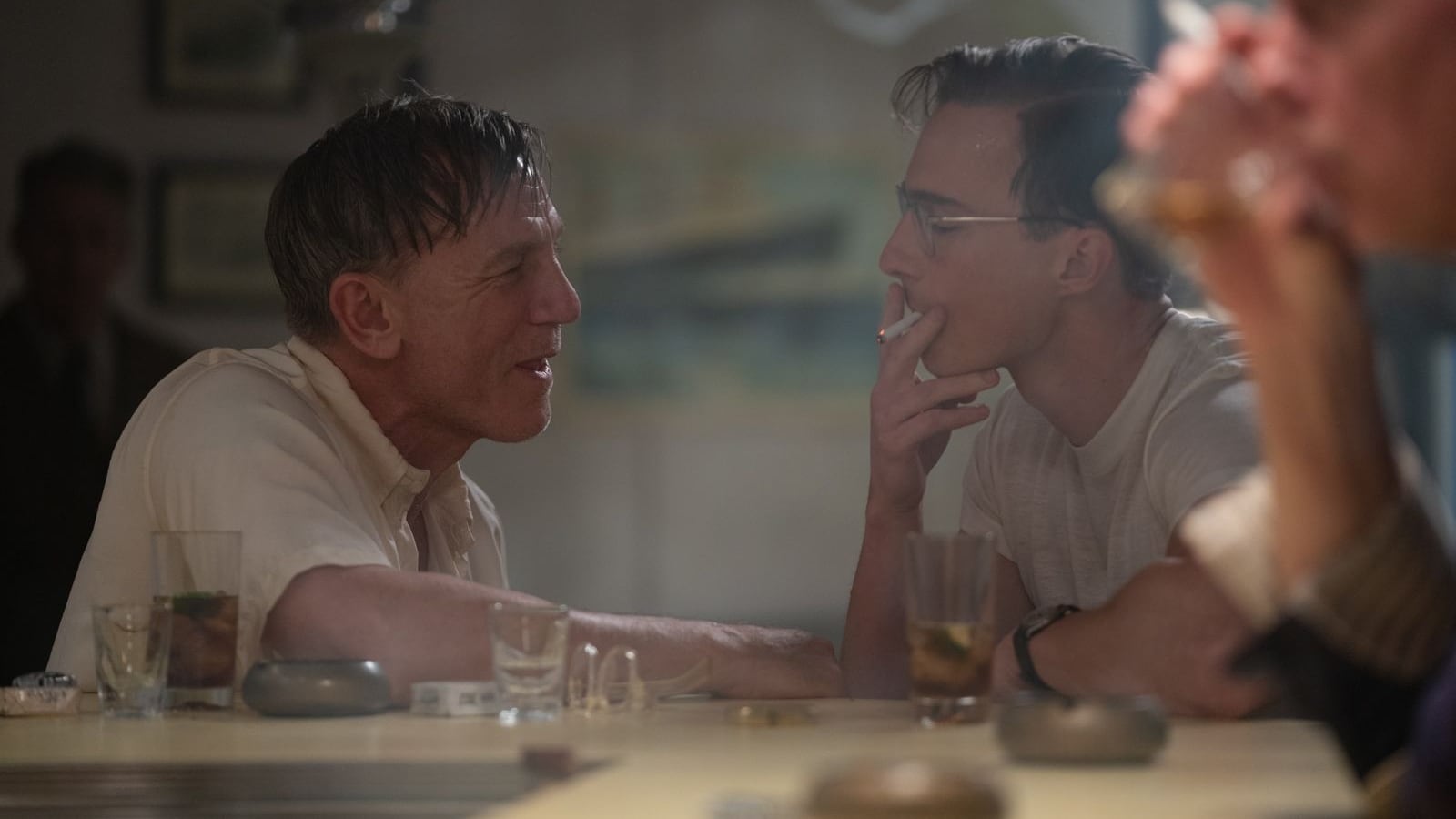 Escena de la película 'Queer' en la que Daniel Craig está sentado en la barra de un bar frente a Drew_Starkey, quien fuma un cigarrillo.