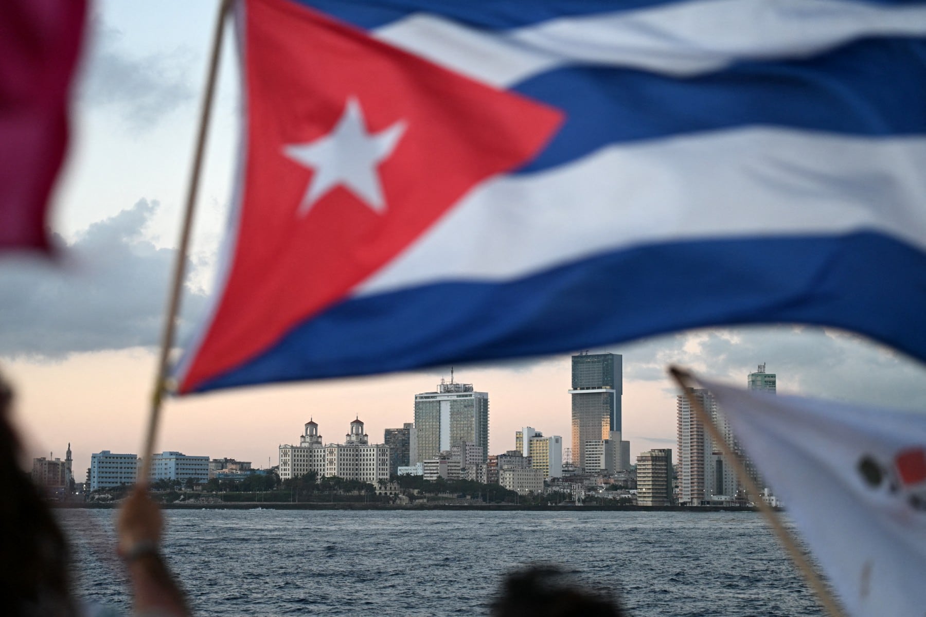 An activist waves a Cuban flag on board the vessel Maguro -- symbolically renamed "Granma 2.0" as a tribute to the yacht used by Fidel Castro's guerrilla fighters to launch their revolution in 1956 -- as it arrives from Mexico with humanitarian aid as part of the Nuestra America convoy, docking at the port of Havana on March 24, 2026. The first boat of a flotilla carrying medical supplies, food and solar panels reached Cuba on March 24, 2026 to aid the island as a US fuel blockade deepens its energy crisis. The Maguro shrimp fishing boat docked in Havana three days later than hoped after battling strong winds, currents and a pesky battery, with two other ships due to follow. (Photo by YURI CORTEZ / AFP)