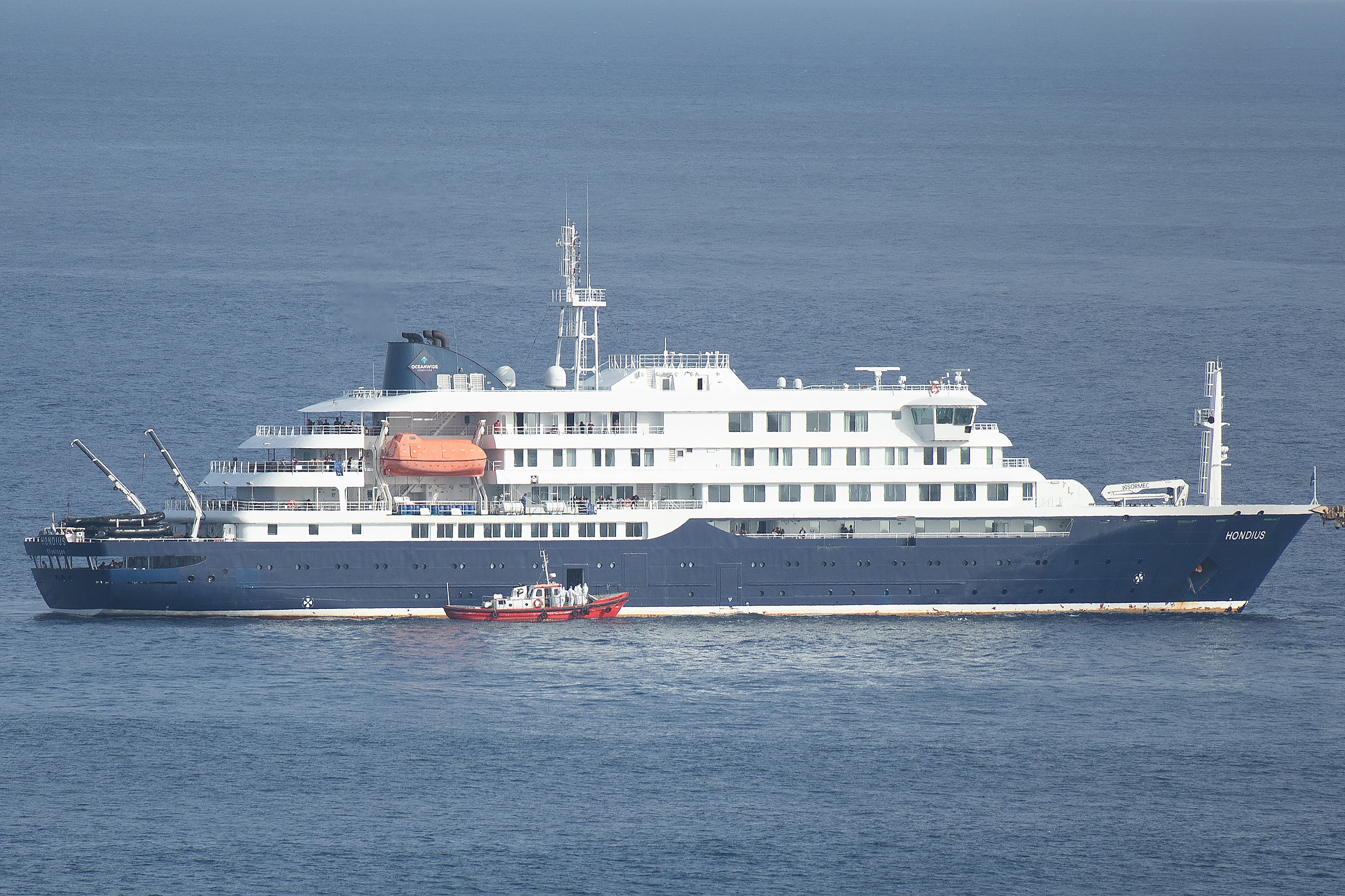 Una lancha ambulancia con tripulantes vestidos con trajes de protección se acerca a la puerta del piloto en el lado de estribor del crucero MV Hondius