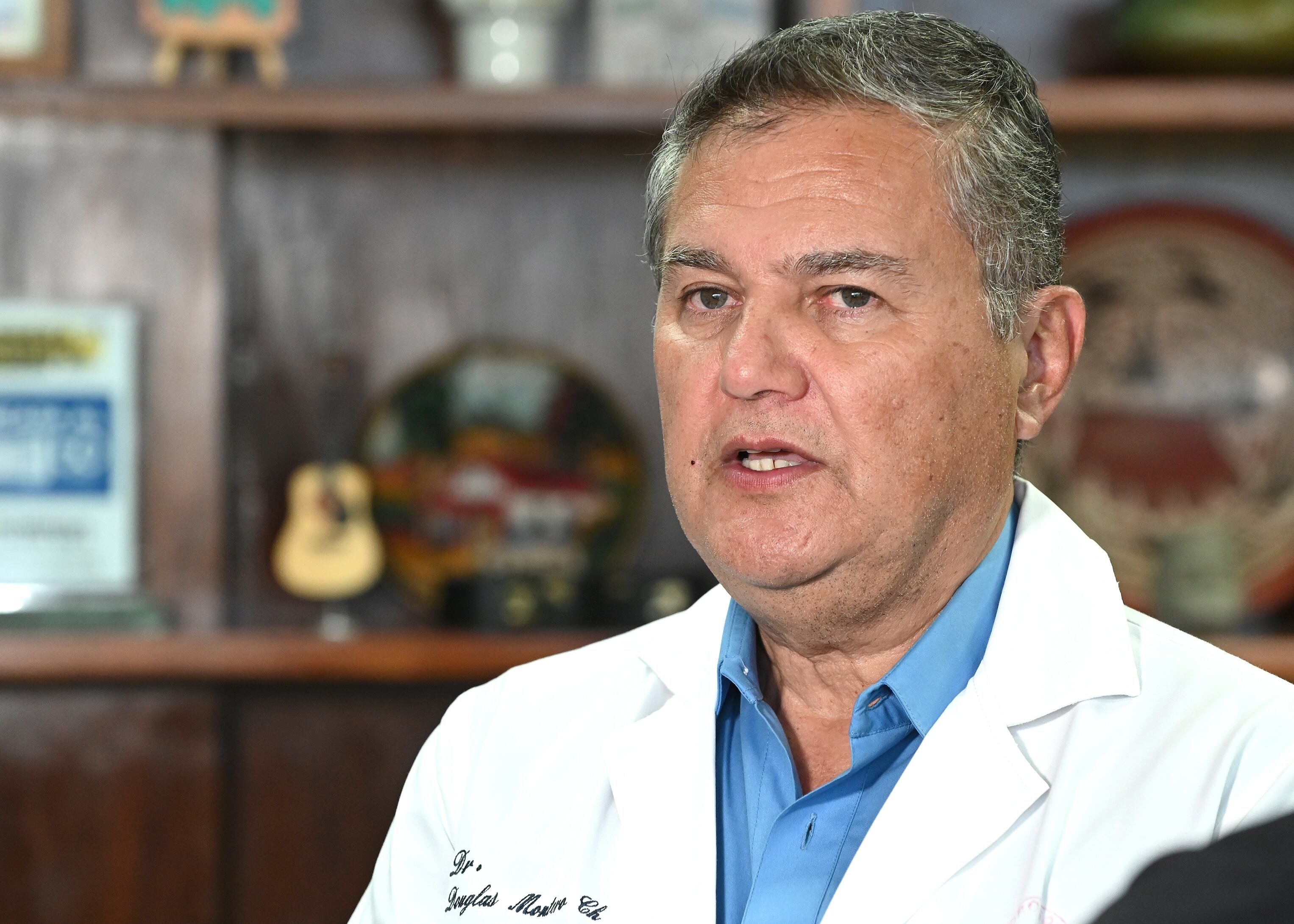 Retrato de hombre maduro, blanco, ojos celestes, canas. Viste gabacha de médico, camisa celeste.