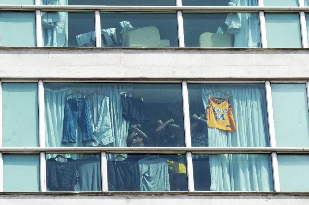 Migrants deported from the US gesture as they look out the window of the Decapolis Hotel where they are temporarily staying in Panama City, on February 18, 2025. (Photo by ARNULFO FRANCO / AFP)