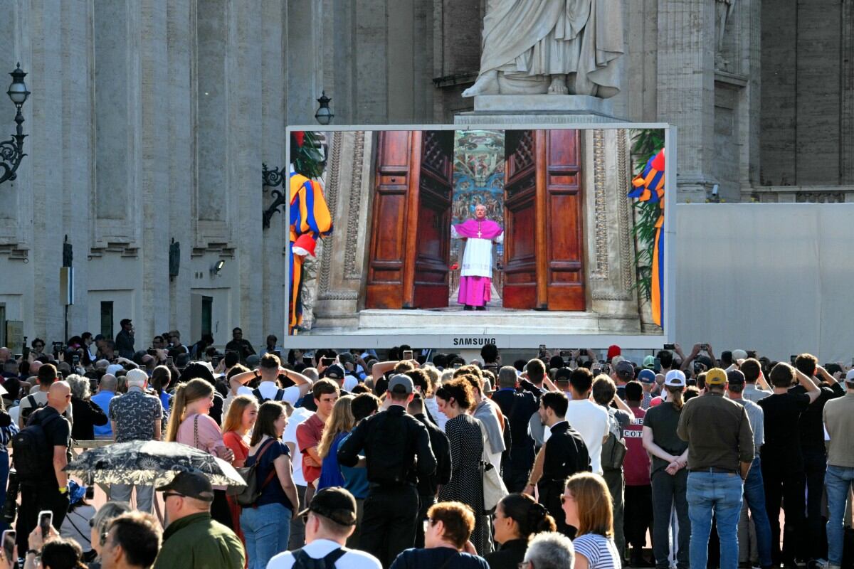 Fieles observan una pantalla gigante que muestra imágenes de Diego Giovanni Ravelli, Maestro de las Celebraciones Litúrgicas Pontificias, cerrando las puertas de la Capilla Sixtina al comenzar el cónclave para elegir a un nuevo Papa, en la Plaza de San Pedro, en el Vaticano, el 7 de mayo de 2025. (Foto de Andreas SOLARO / AFP)