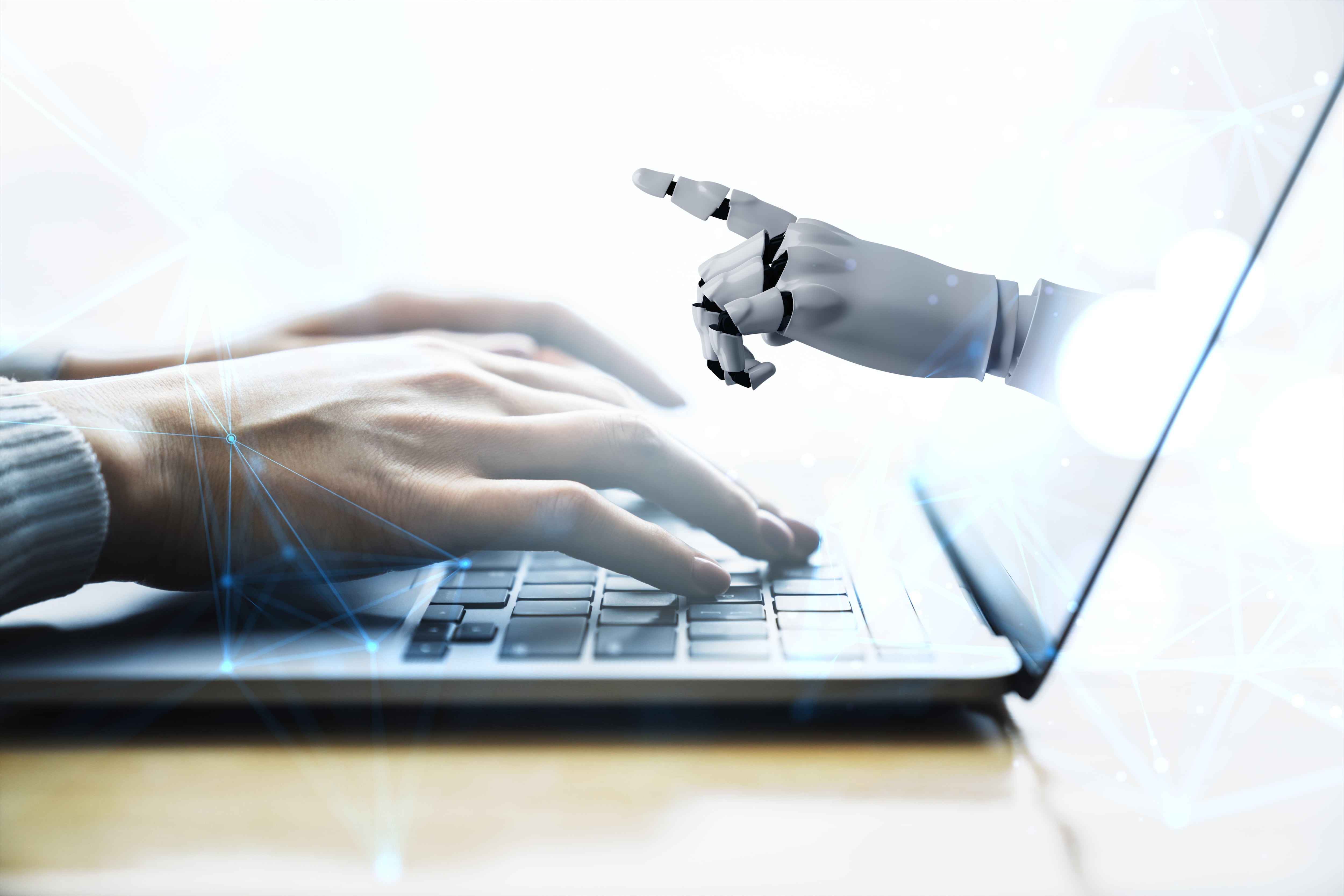 Manos humanas teclean sobre una laptop y de su pantalla sale una mano de robot que apunta al usuario. IA, inteligencia artificial