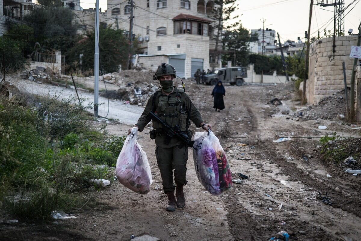 Un soldado israelí carga las posesiones de una mujer en la Cisjordania ocupada por Israel.