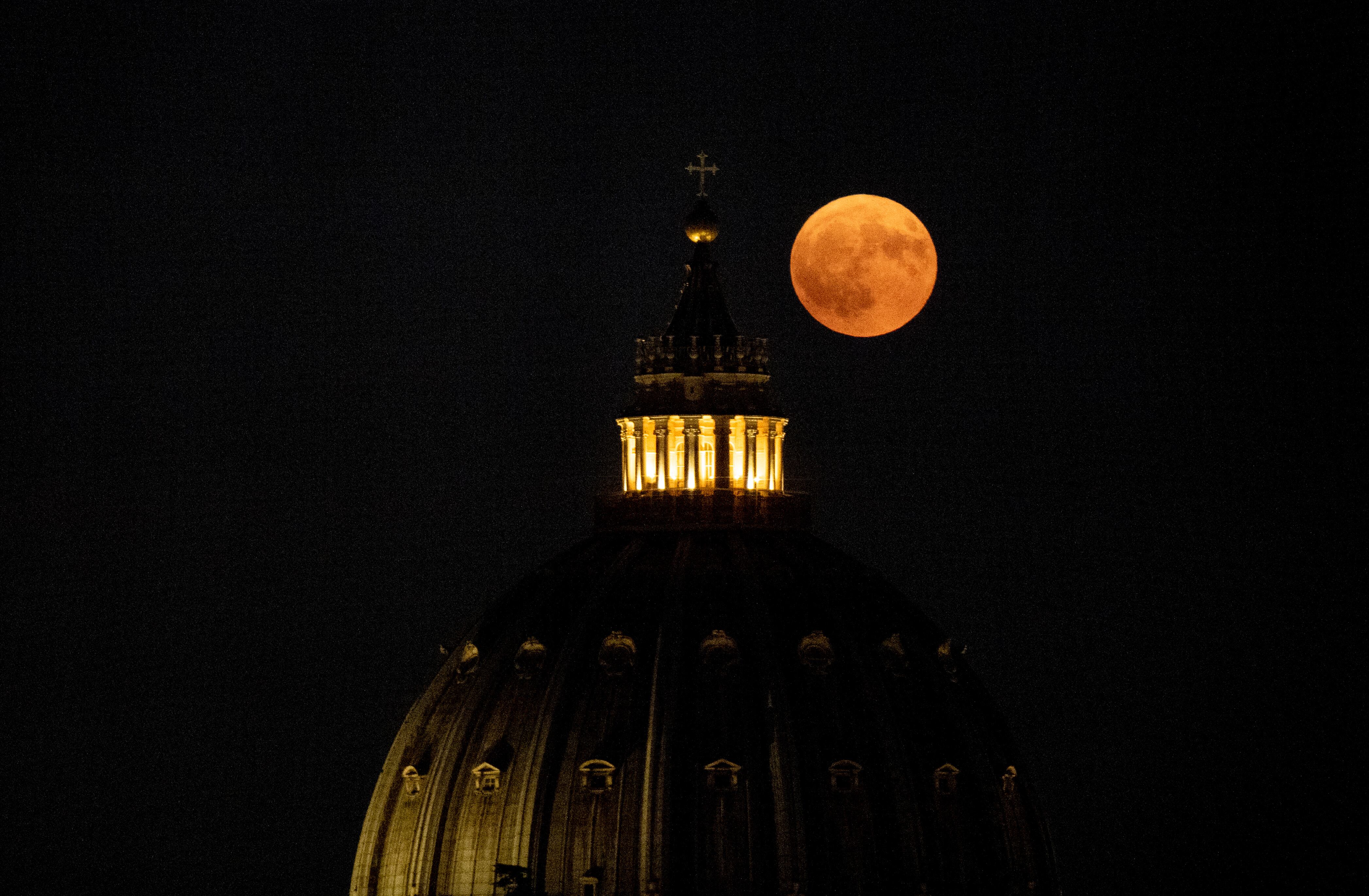 This photograph taken in Rome shows the Super Blue Moon rising over the dome of St Peter's Basilica in the Vatican City, on August 19, 2024. (Photo by Tiziana Fabi / AFP)