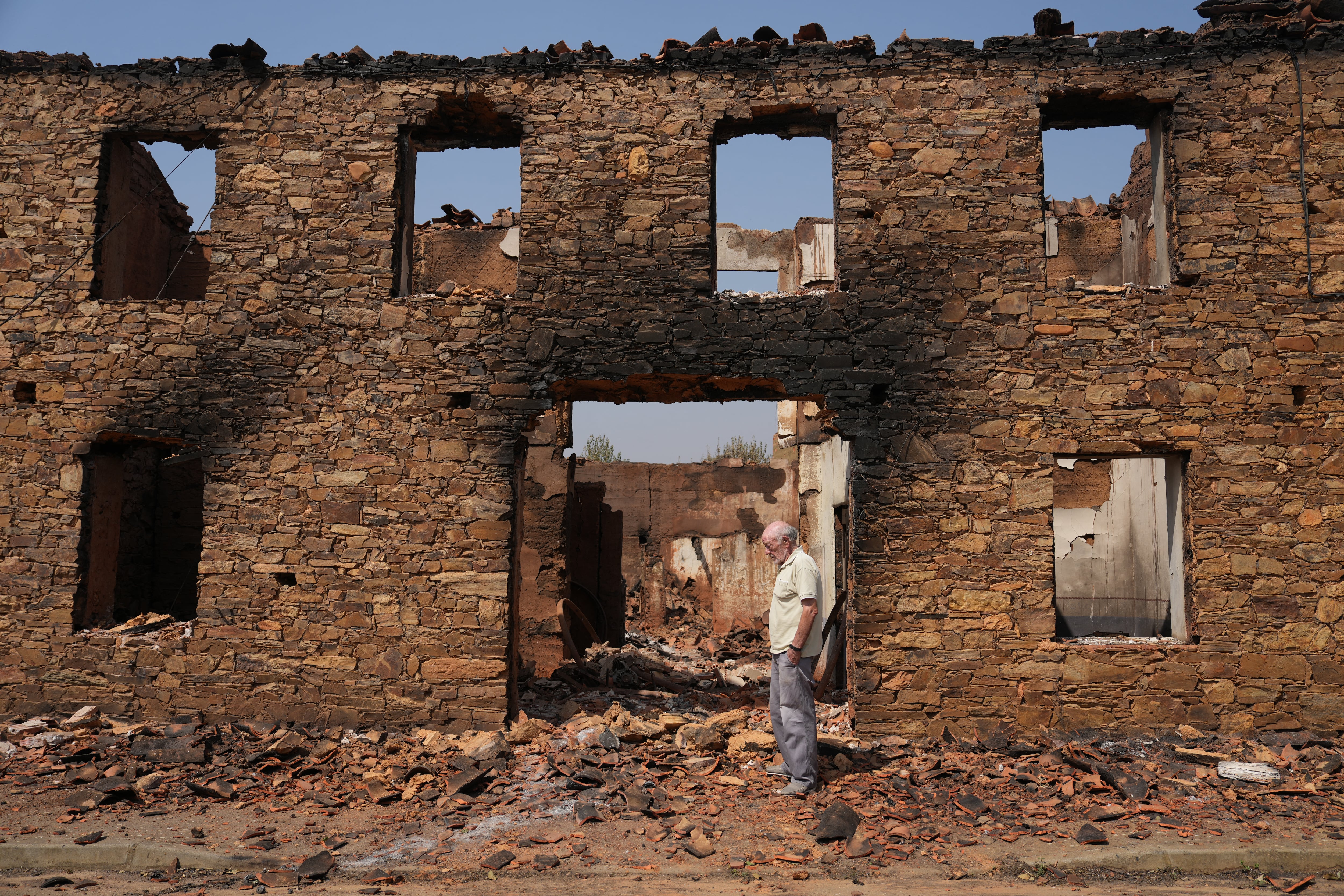 A man stands in front of a burnt house in ruins after a wildfire in the village of Castrocalbon, northwestern Spain, on August 16, 2025. Spain, now in its third week under a heatwave alert, is still battling wildfires raging in the northwest and west of the country, where the army has been deployed to help contain the blazes. The regions of Castilla y Leon, Galicia, Asturias and Extremadura remain the hardest hit. (Photo by Cesar Manso / AFP)