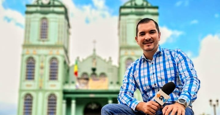 El periodista José Ernesto Herrera mientras trabajaba en Más que noticias. Está sentado frente a una iglesia y sostiene un micrófono.