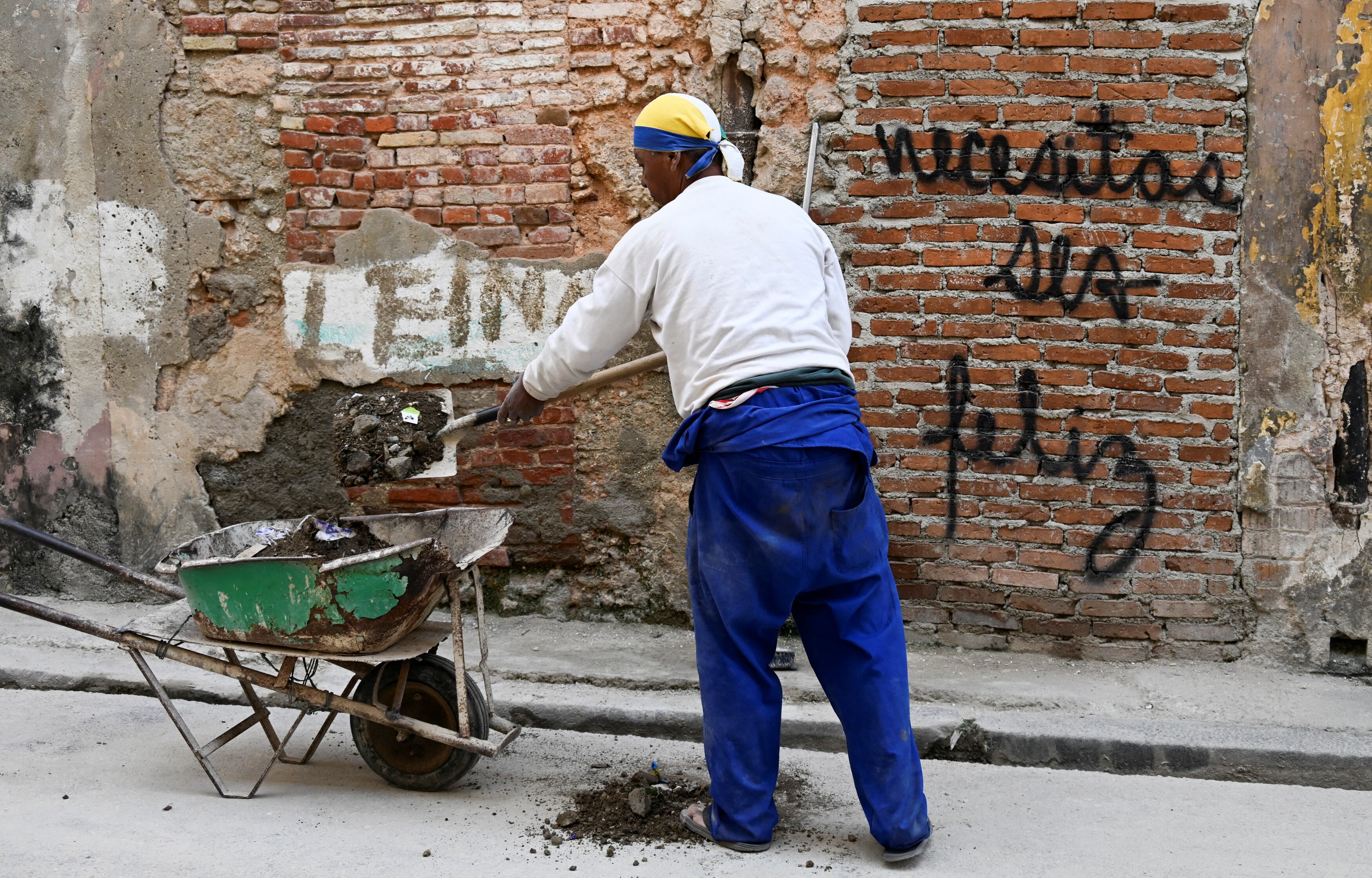 Trabajador junto a un muro en La Habana con un grafiti que dice "Necesitas ser feliz", obra del artista cubano Mr. Sad.