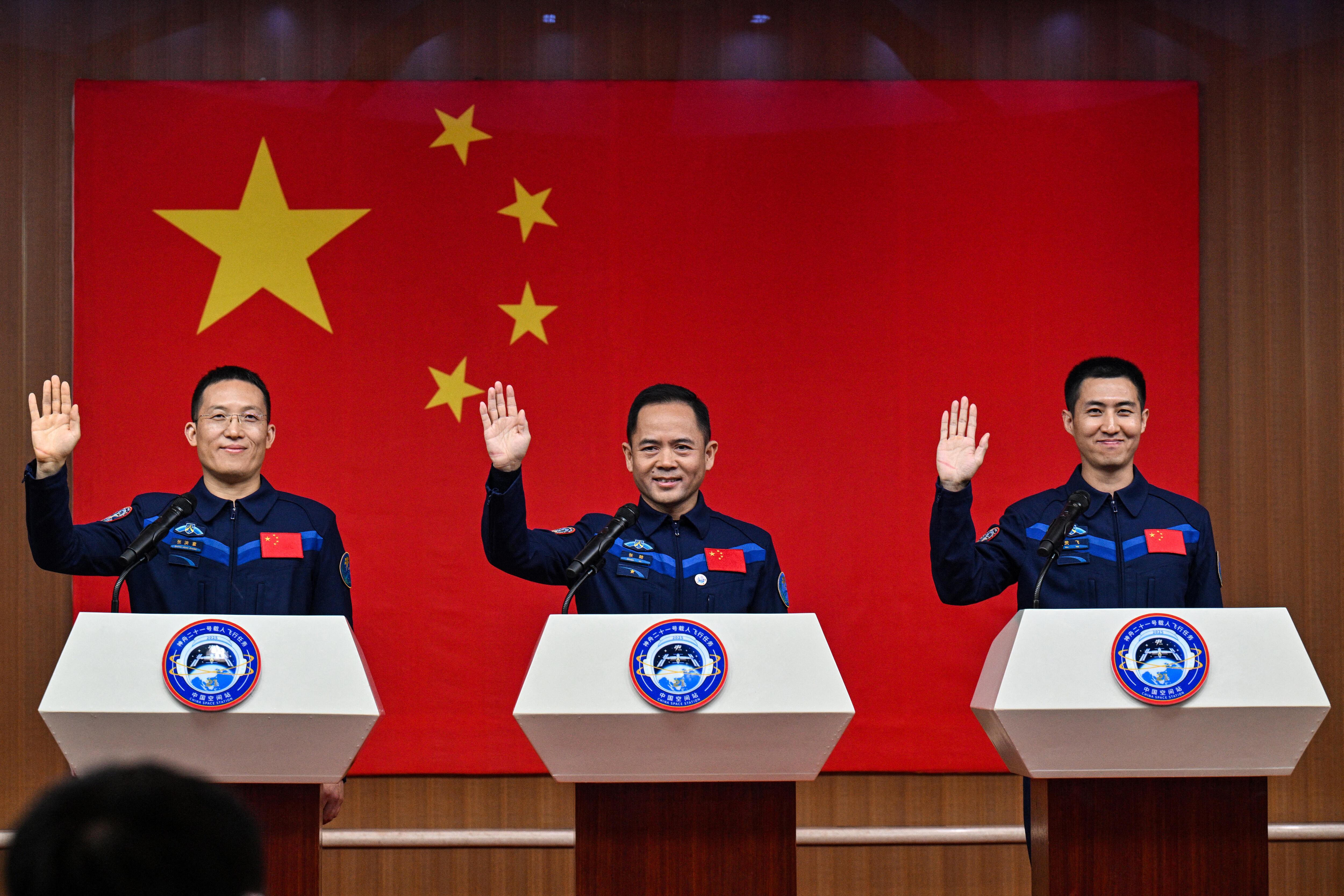 Los astronautas de la misión espacial china Shenzhou-21, Zhang Hongzhang (izquierda), el comandante Zhang Lu (centro) y Wu Fei (derecha), saludan durante una conferencia de prensa celebrada el día antes del lanzamiento de la misión en el Centro de Lanzamiento de Satélites de Jiuquan, en el desierto de Gobi, al noroeste de China, el 30 de octubre de 2025. (Foto de Héctor RETAMAL / AFP)