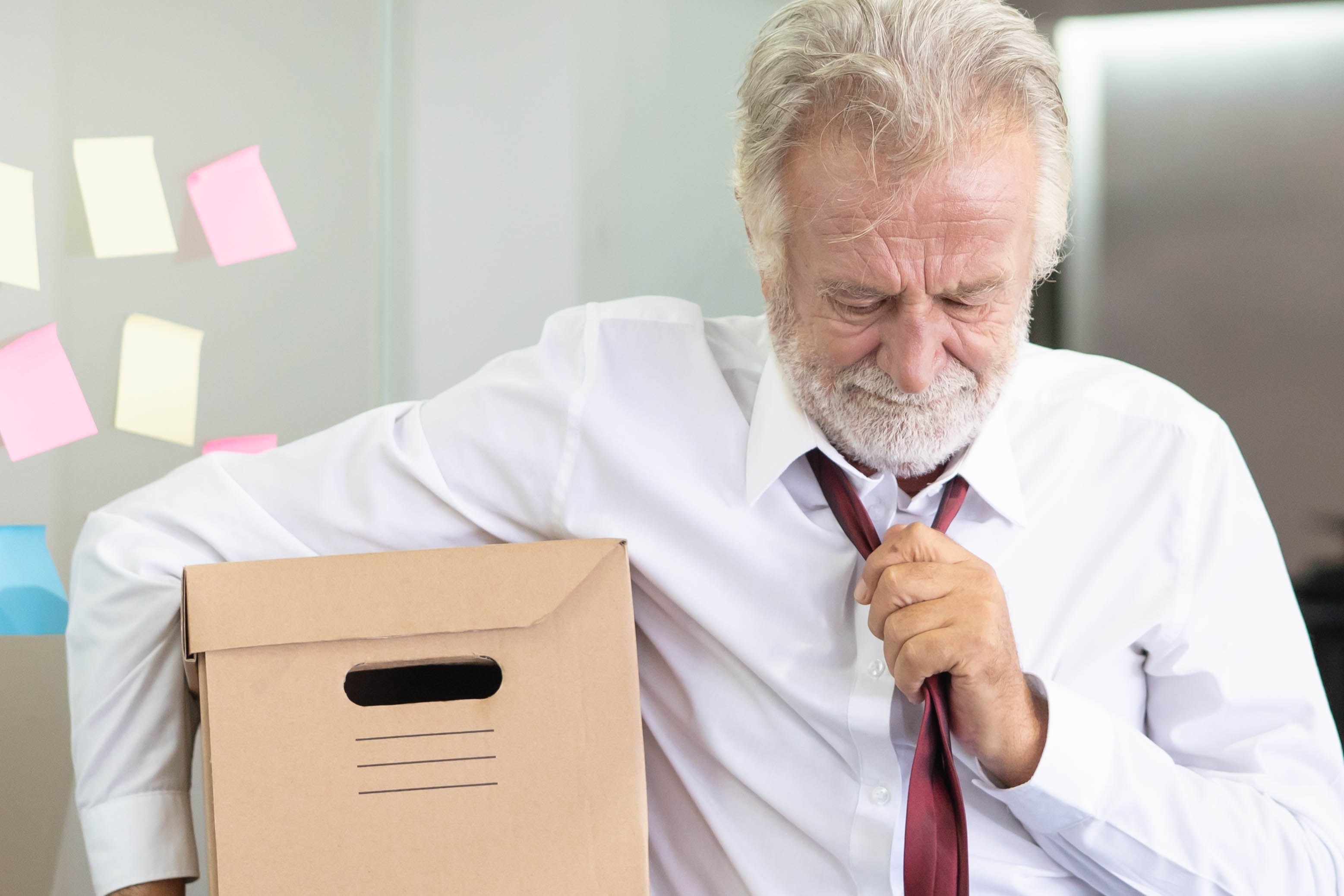 Despidos por edad, despedido del trabajo, discriminación laboral por edad, edadismo, talento sénior, desempleo por edad, desprecio a la experiencia, canas, hombre canoso sale de la oficina con caja
