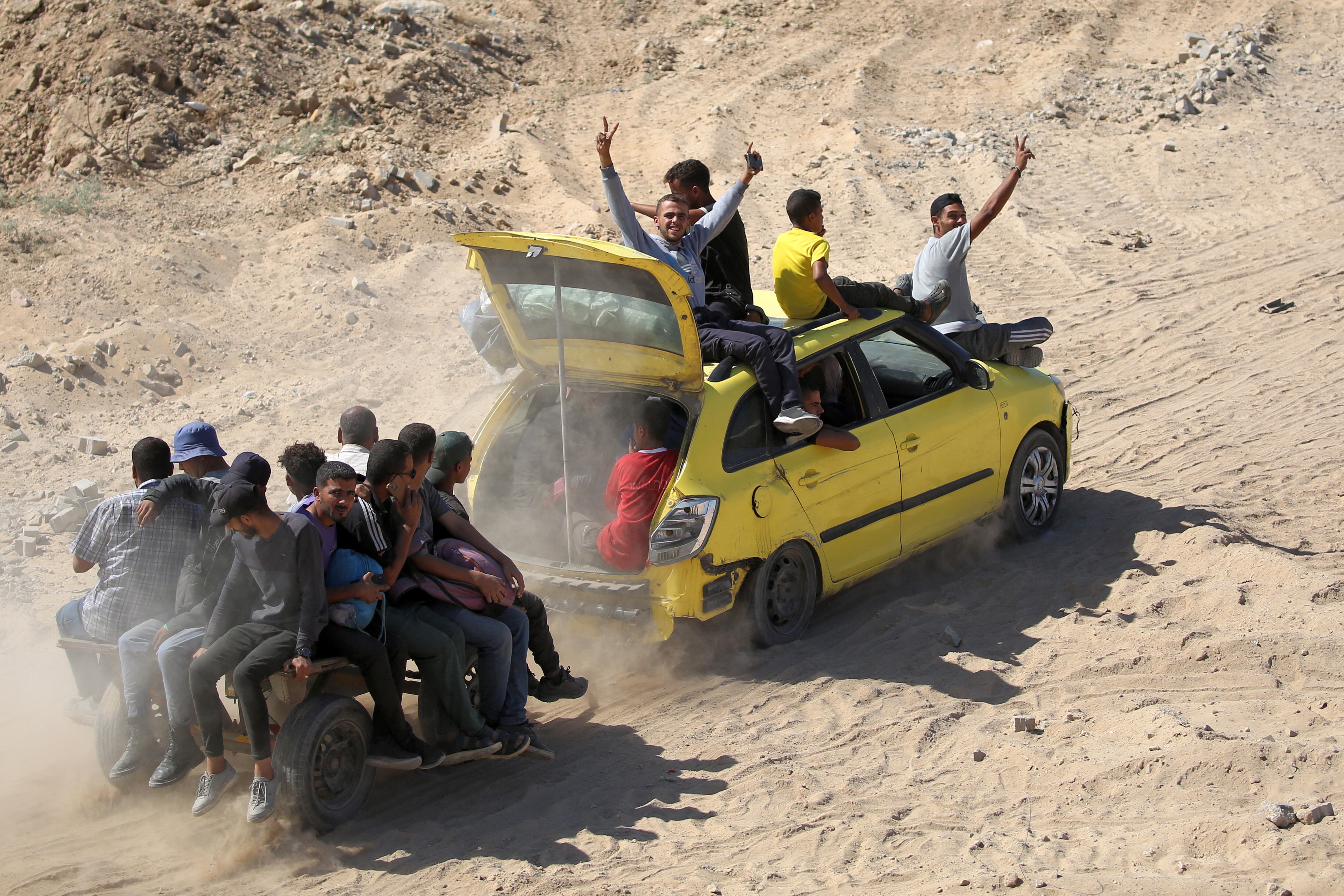Hombres hacen gestos sentados sobre un vehículo que remolca otro carro con pasajeros, avanzando por un camino de tierra hacia la ciudad de Gaza, cerca de Nuseirat, en el centro de la Franja de Gaza, el 10 de octubre de 2025.