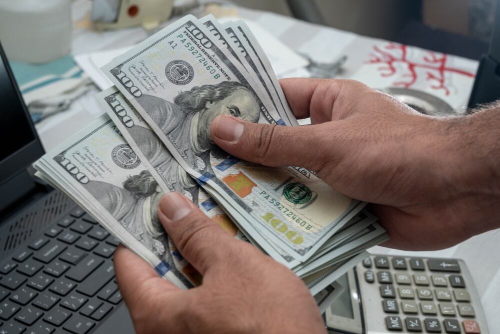 Manos contando billetes de $100 sobre una mesa con una calculadora, representando el movimiento del tipo de cambio del dólar en Costa Rica durante enero de 2025.