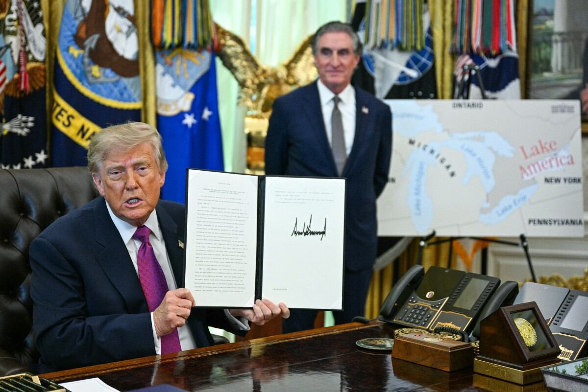 El presidente de Estados Unidos, Donald Trump, acompañado por el secretario del Interior, Doug Burgum, muestra una orden ejecutiva que firmó para cambiar el nombre del lago Ontario por lago América, en el Despacho Oval de la Casa Blanca, en Washington D. C., el 27 de agosto de 2026.