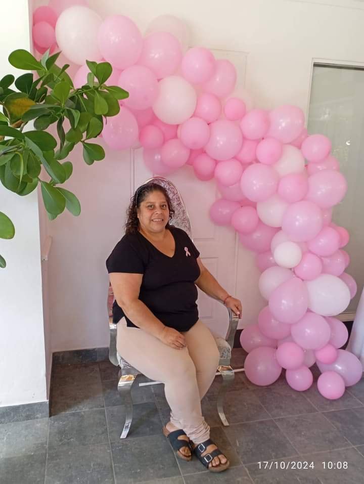 Una mujer sentada en una silla. Hay globos rosados al fondo.