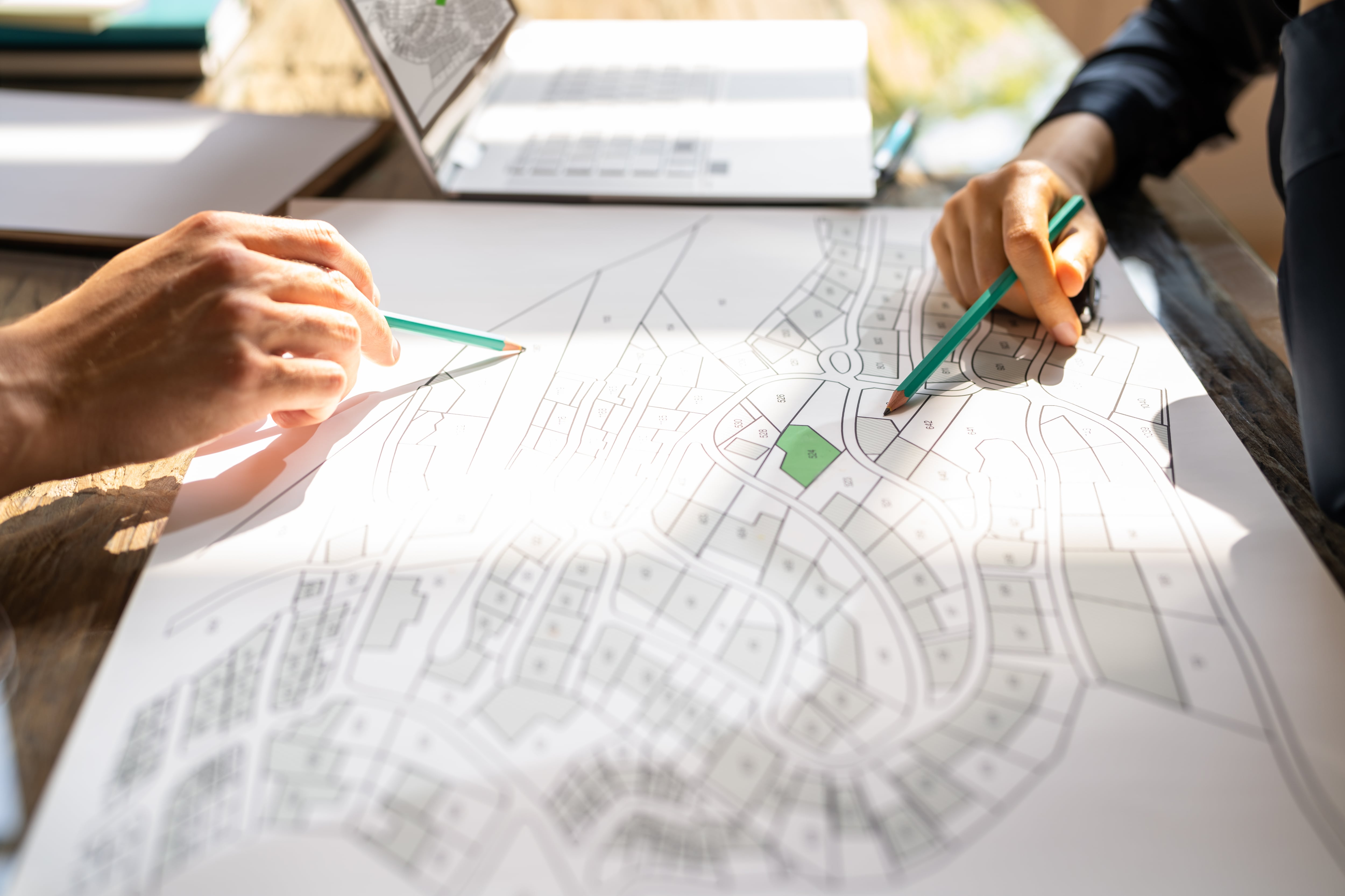 Primer plano de manos con lápices sobre plano de urbanización y zona verde