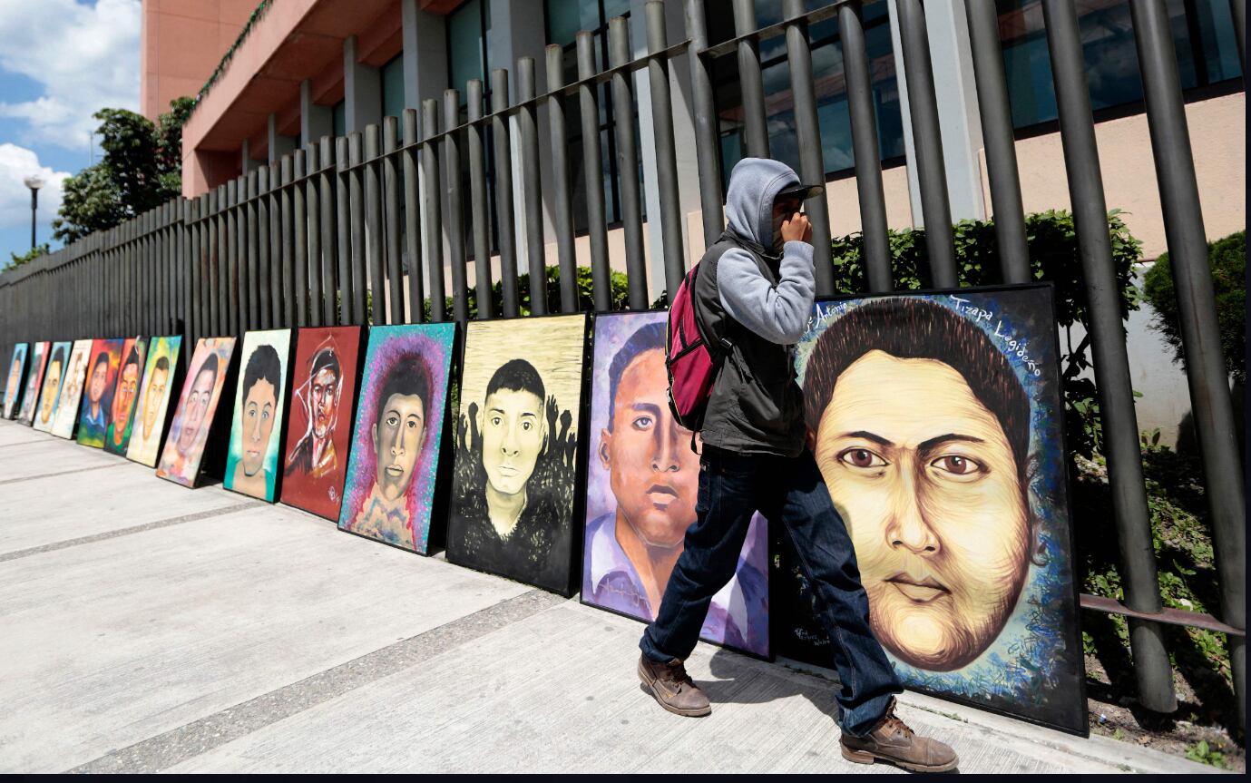 Estudiante pasa junto a los retratos de los 43 estudiantes desaparecidos de Ayotzinapa frente al Congreso de Guerrero en Chilpancingo, México, en 2015.