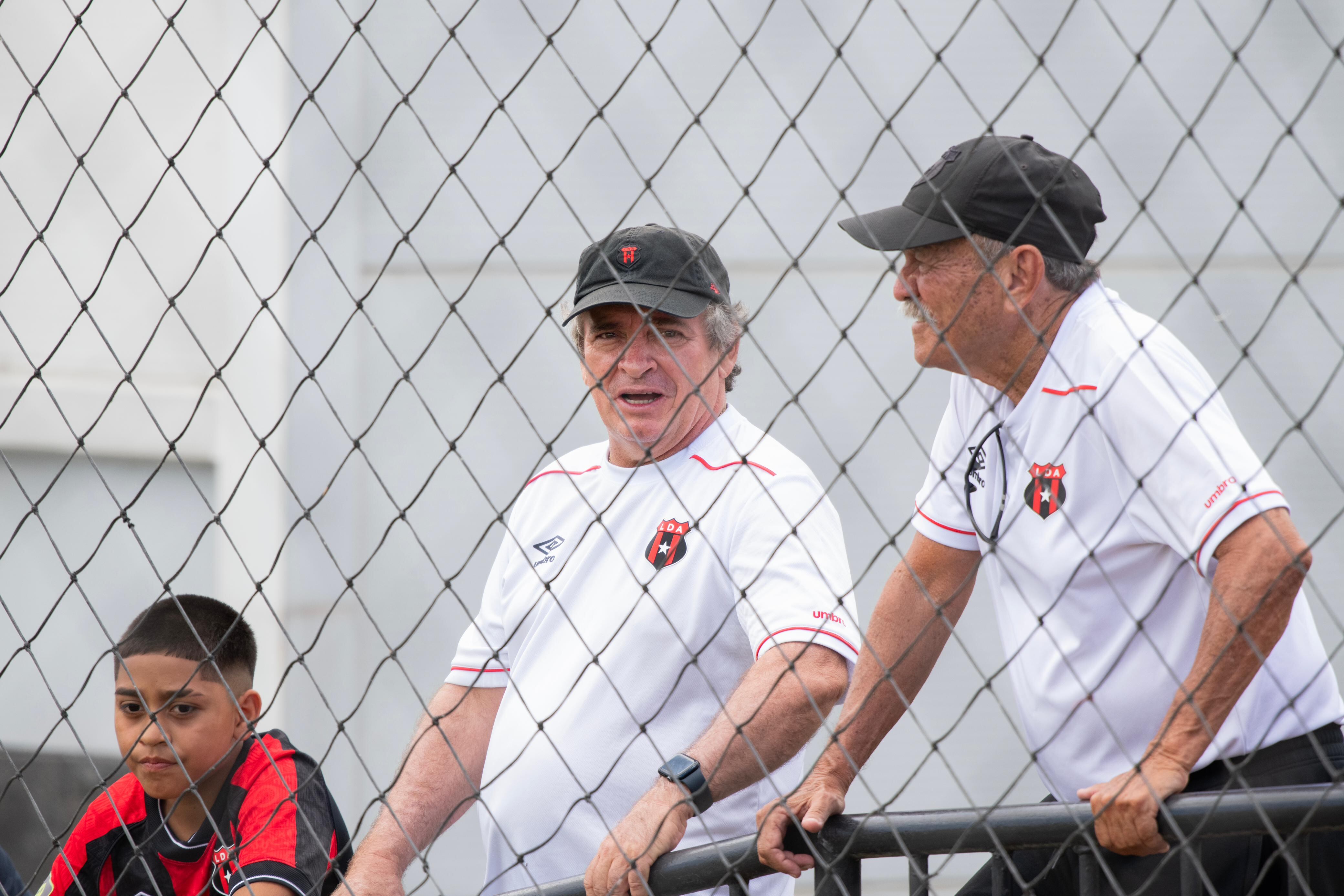 Óscar Ramírez conversa con Enrique Vásquez mientras observan un partido de liga menor de Liga Deportiva Alajuelense.