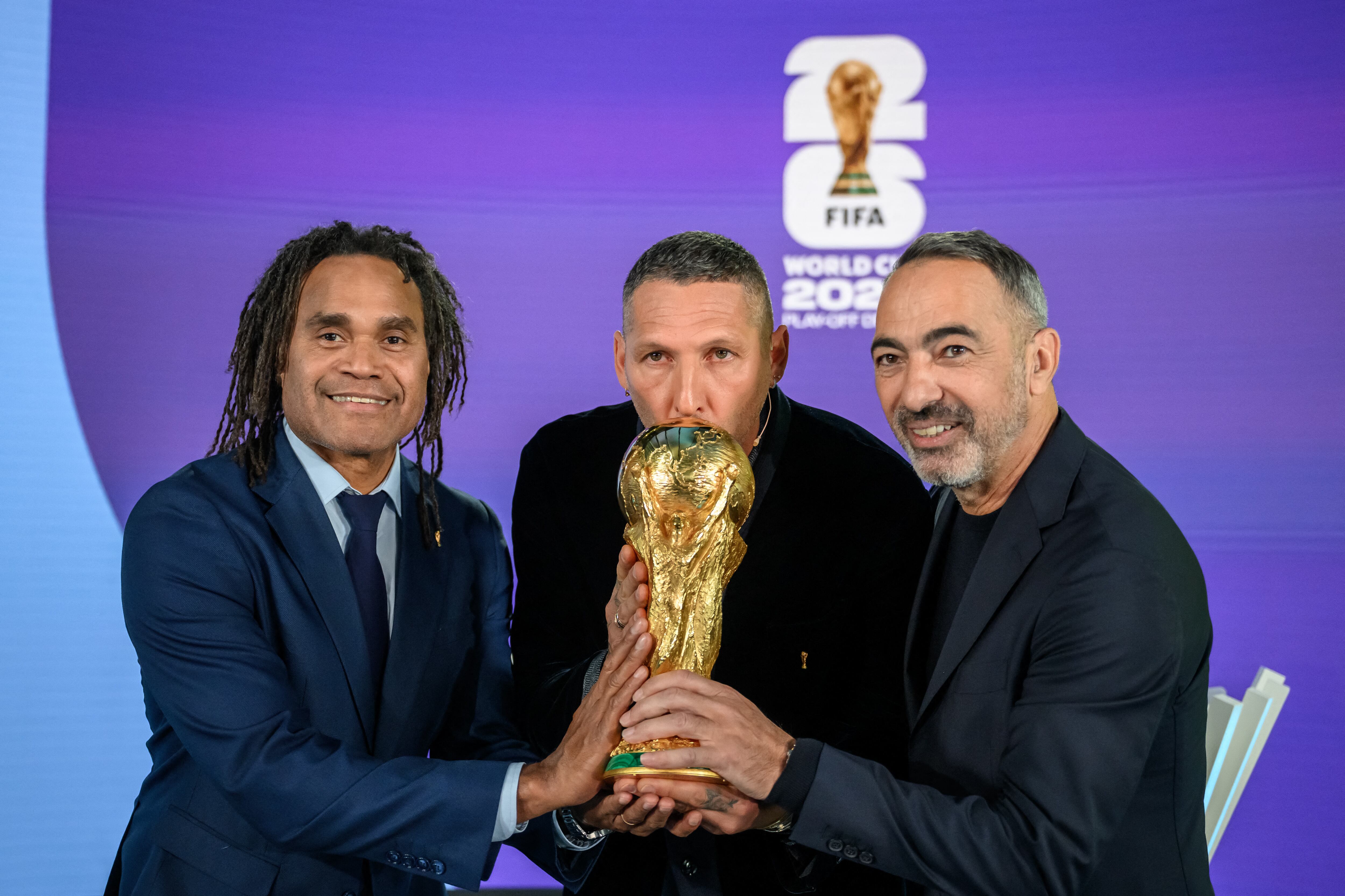Los exjugadores Christian Karembeu de Francia, Marco Materazzi de Italia y Youri Djorkaeff de Francia posan con el trofeo del Mundial, durante el sorteo de FIFA para la repesca europea.