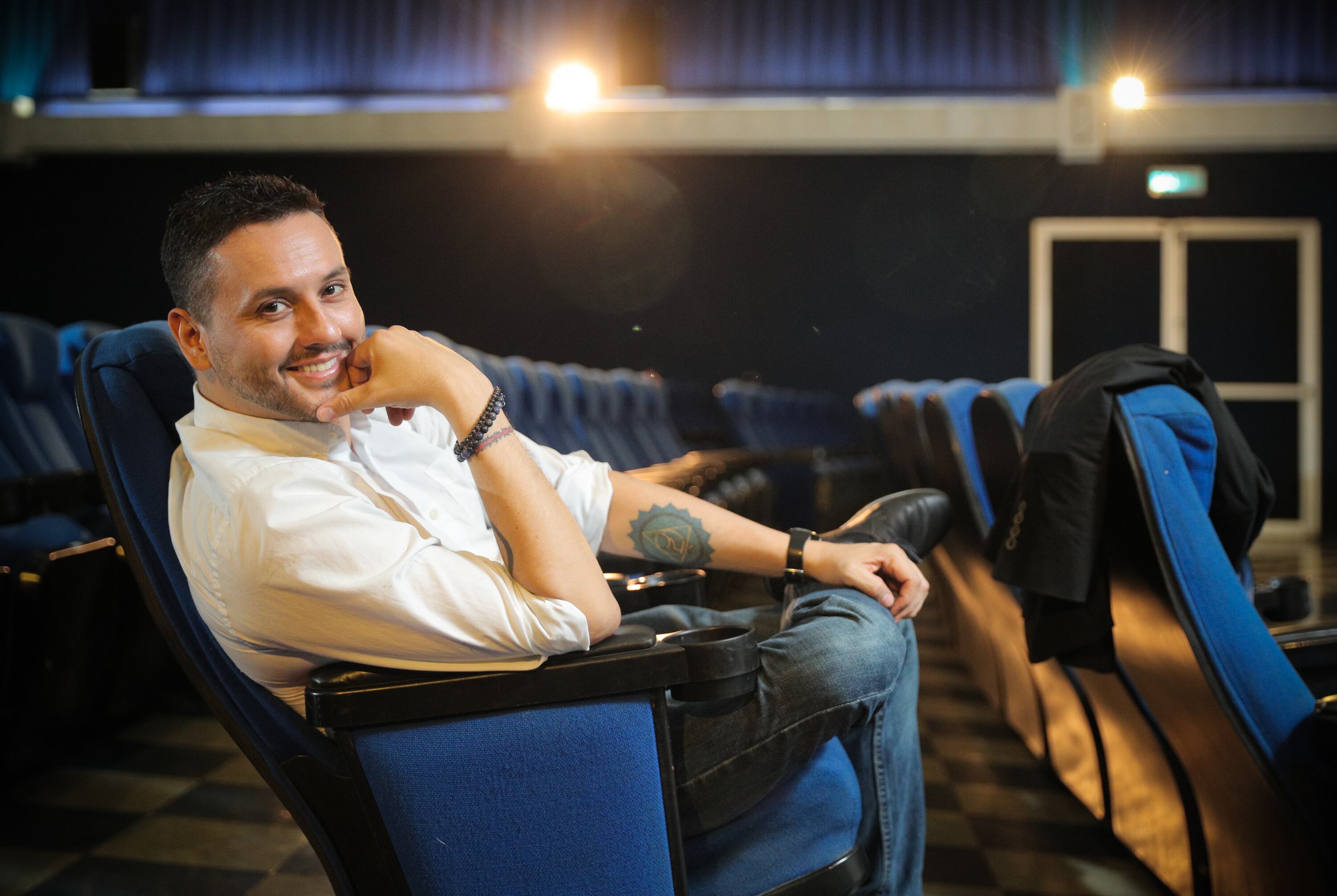 Retrato de Walter Campos sentado en una butaca de cine. Usa camisa blanca y jeans.