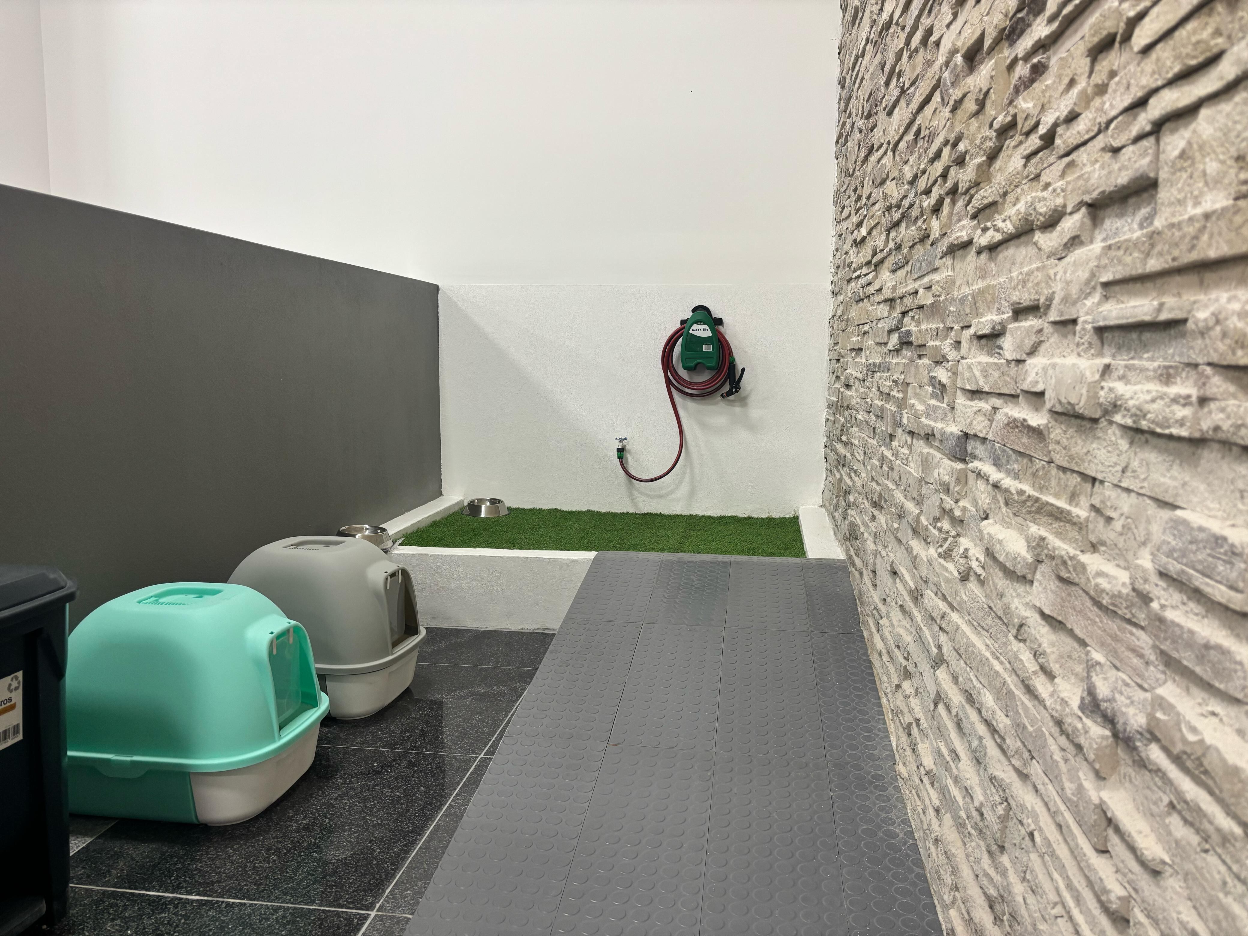 Área para atender a mascotas, aparecen dos jaulas, zacate sintéticos, una manguera