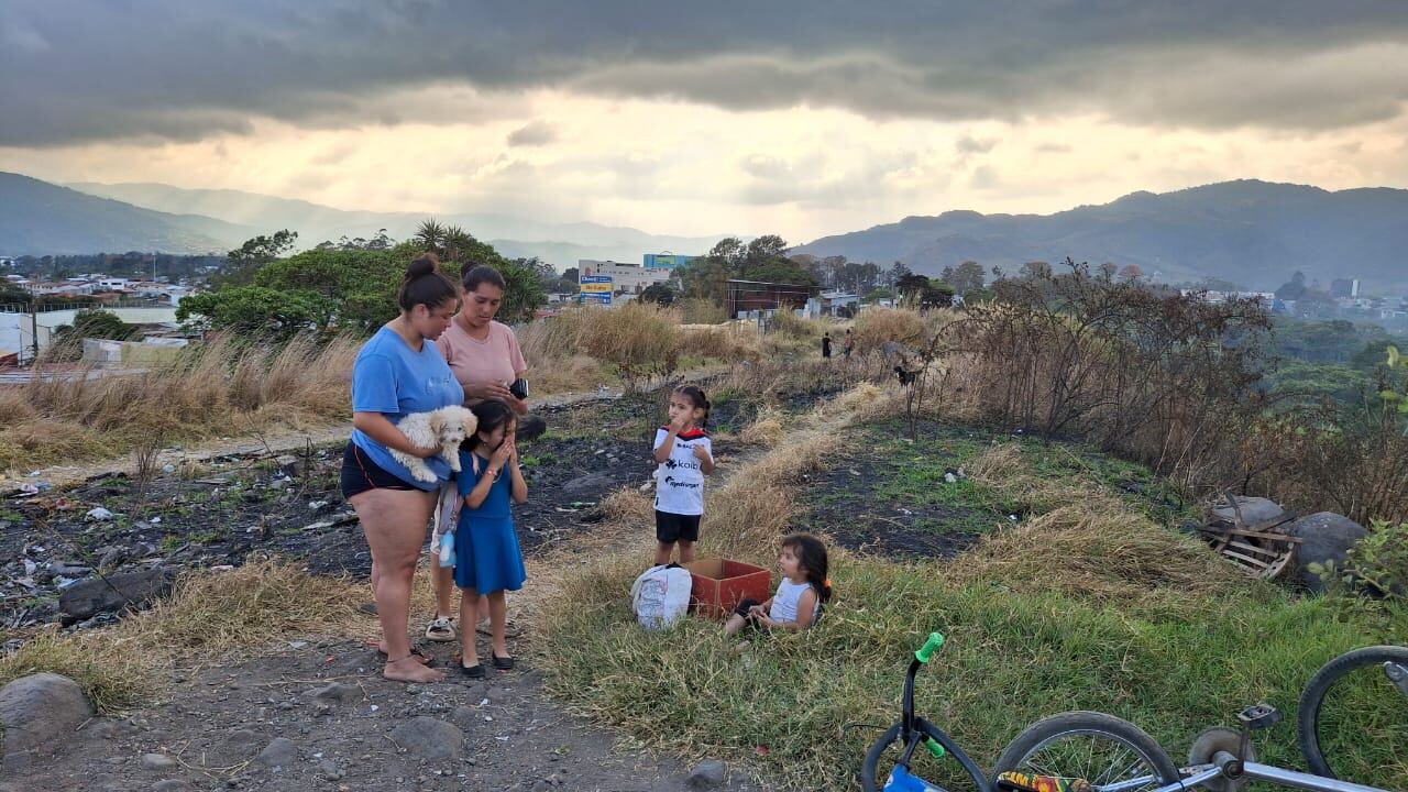 Imagen de dos mujeres y tres niños en un potrero, con montañas y el atardecer de fondo.