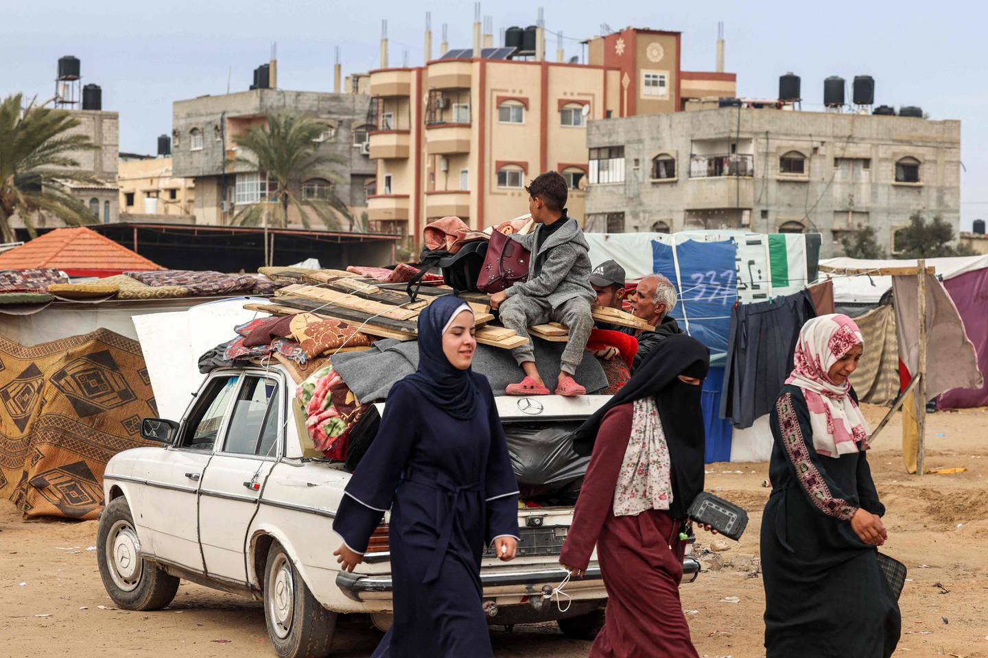 Las mujeres pasan junto a un vehículo cargado con artículos asegurados con cuerdas mientras la gente huye de Rafah hacia el norte, hacia el centro del territorio palestino, en medio del conflicto en curso entre Israel y el grupo militante palestino Hamas. (Foto de MOHAMMED ABED / AFP)